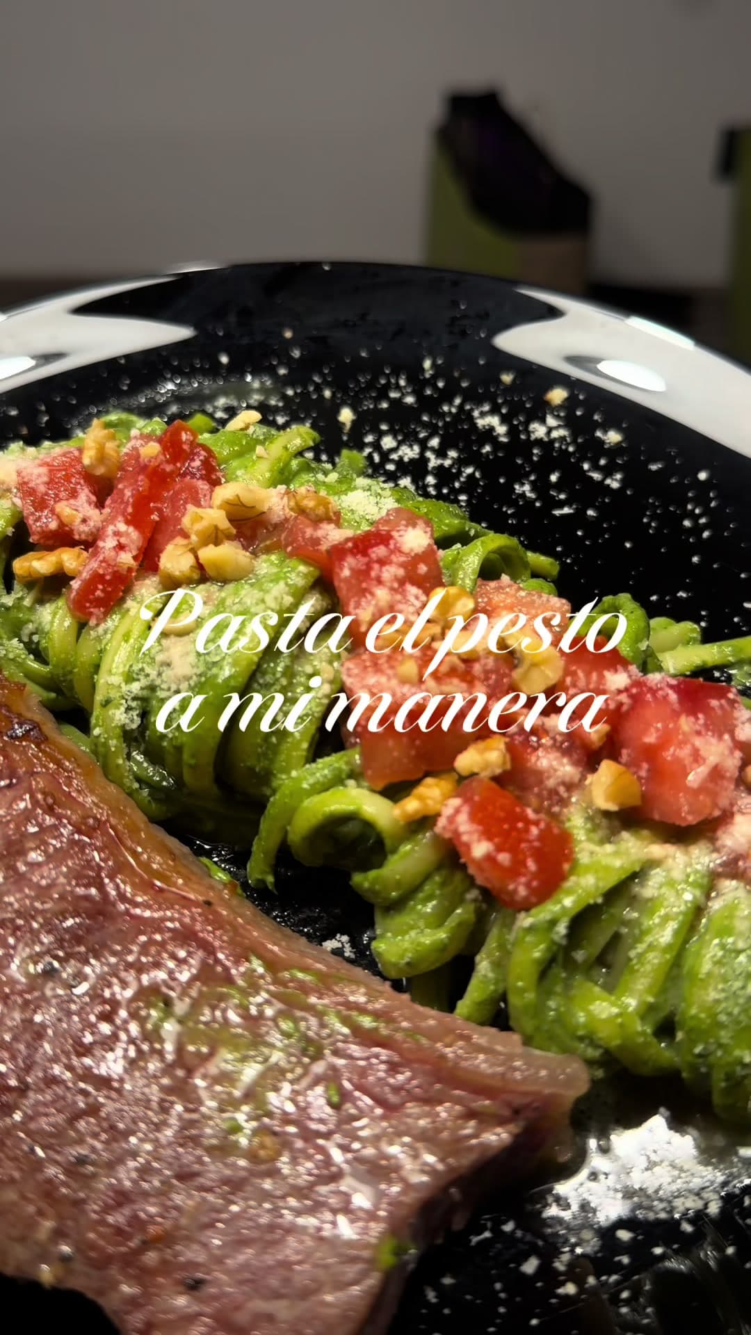 Spaghetti al pesto con tomate picado, nueces y queso rallado, con un lomo a la sartén al lado.